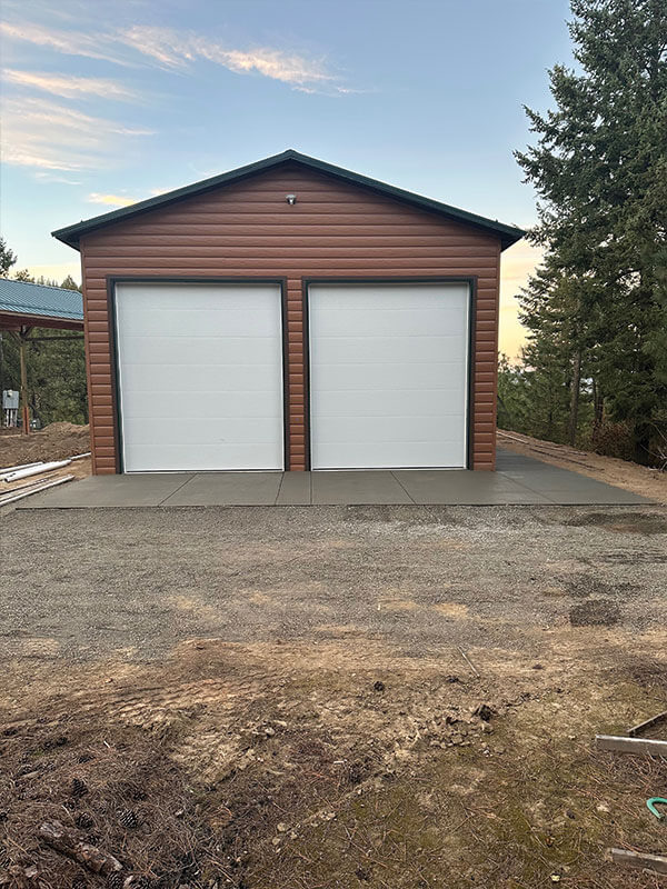 Detached garage with two white overhead doors kept in repair by Gitter Done Construction